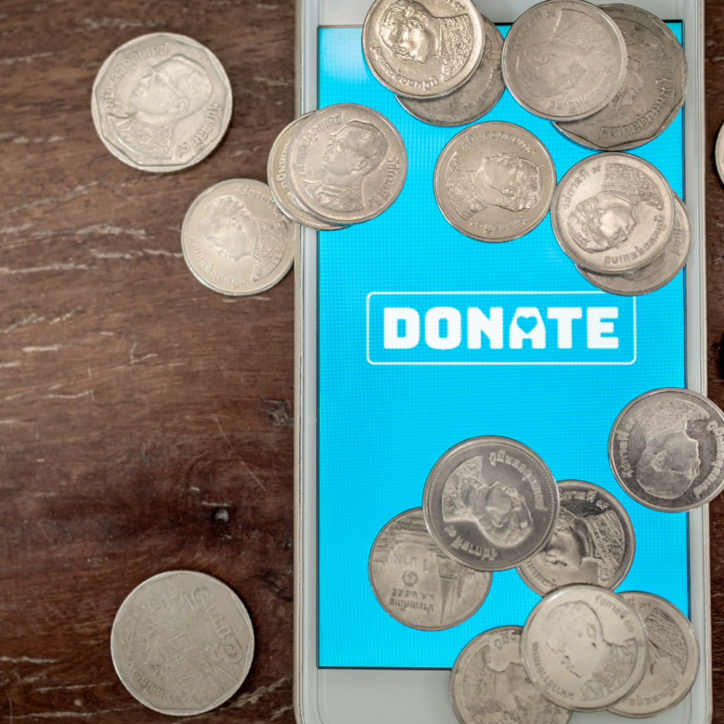 Cellphone with blue backdrop on the screen and the words DONATE. American coins sit on top of the phone